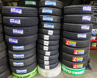 さまざまなメーカーの新品タイヤが積み重なって販売されている写真